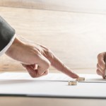 Male hand pushing a wedding ring over to a female hand about to sign divorce papers. Conceptual of divorce or marriage.