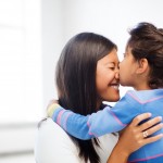 family, children and happy people concept - happy little girl hugging and kissing her mother over white room background