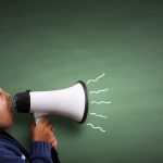 Child speaking through a megaphone against a blackboard with copy space